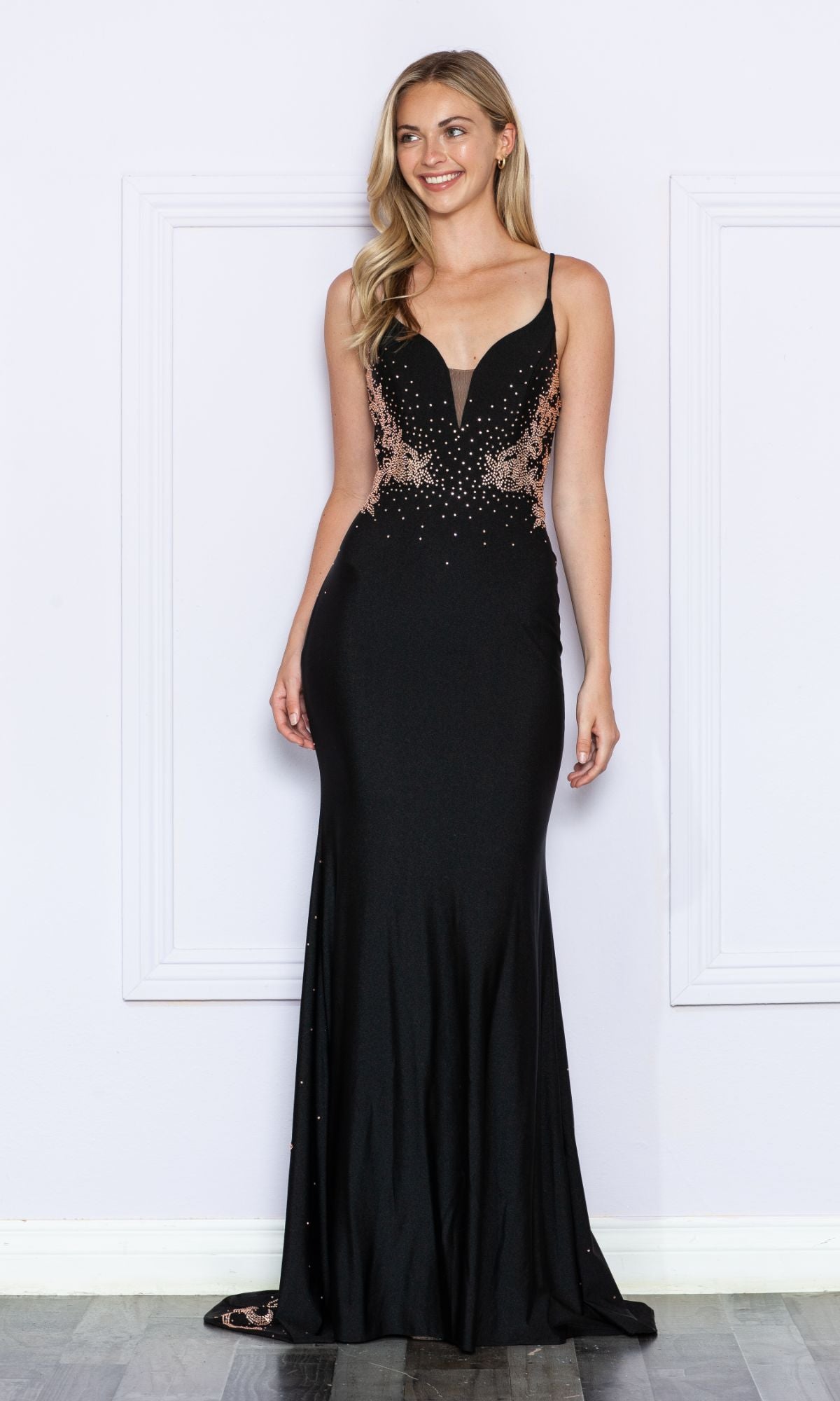 A woman poses against a white wall in the Contrasting Beads Long Black Prom Dress 9274, featuring thin straps and intricate beadwork for a look of classic elegance.